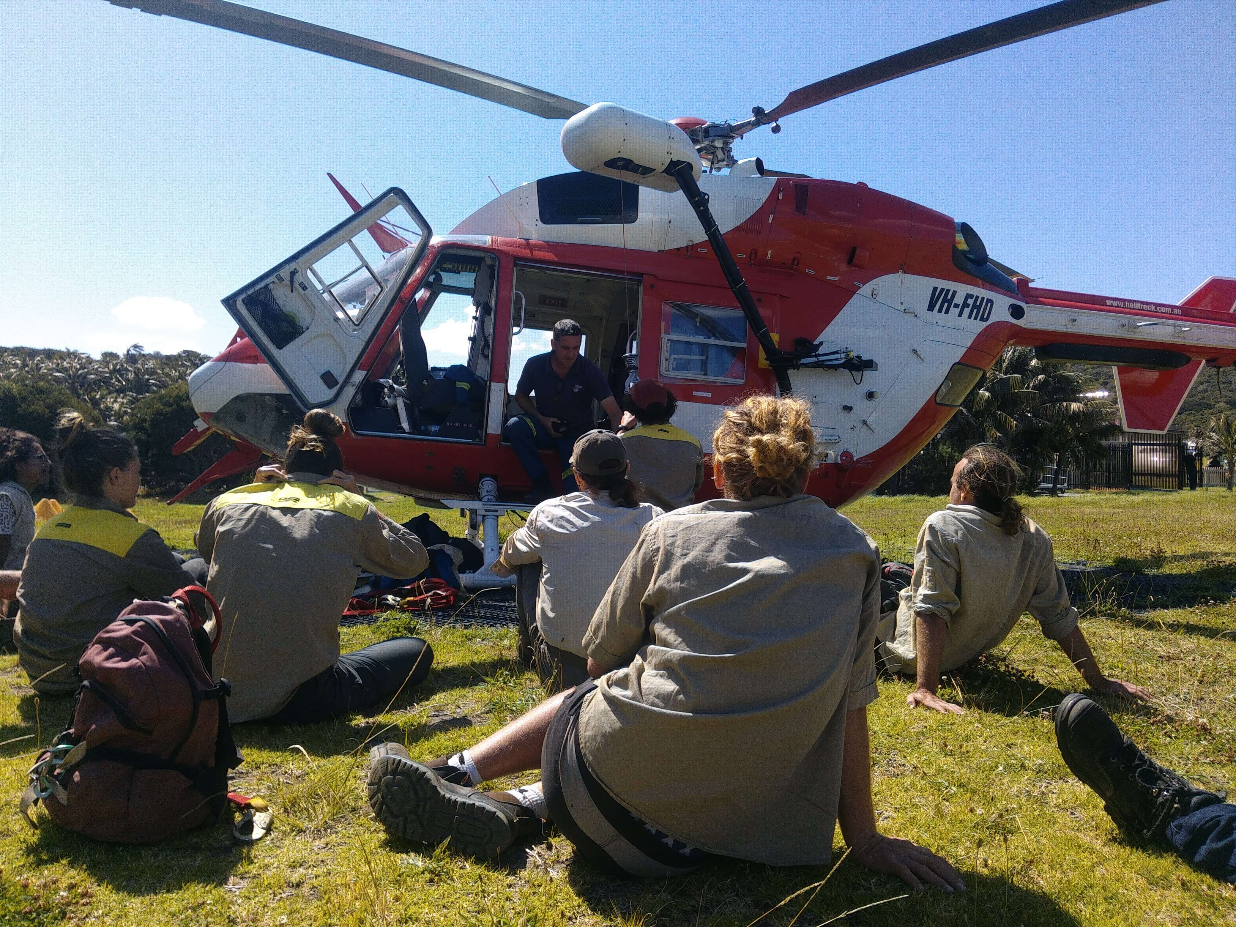 LHIB staff sitting on grass in front of helicopter