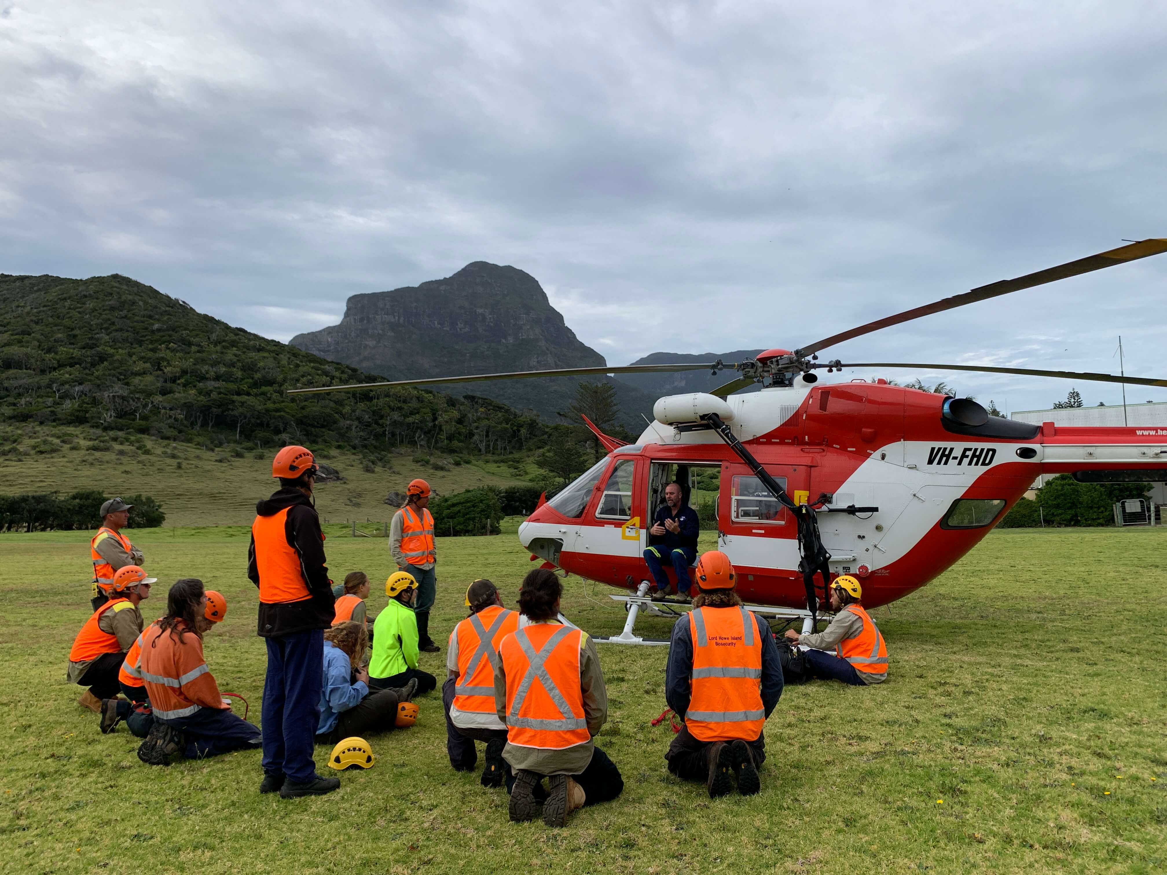 A group of people in orange high-vis vests sitting around a helicopter